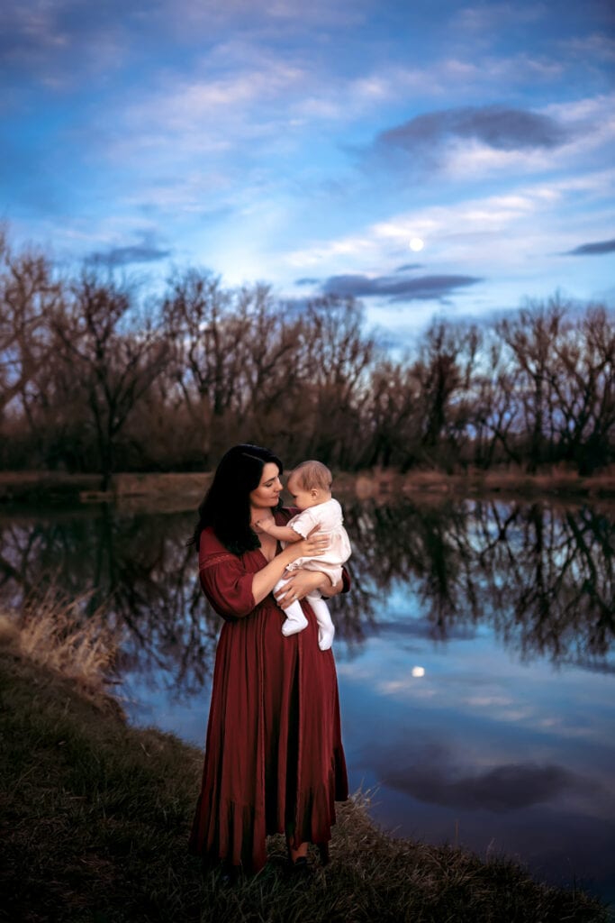 Family Photographer, a mother holds her baby near a lake in the forest