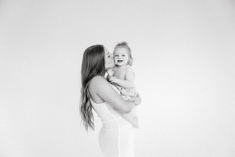 Family Photographer, a woman holds her baby and gives her a kiss inside