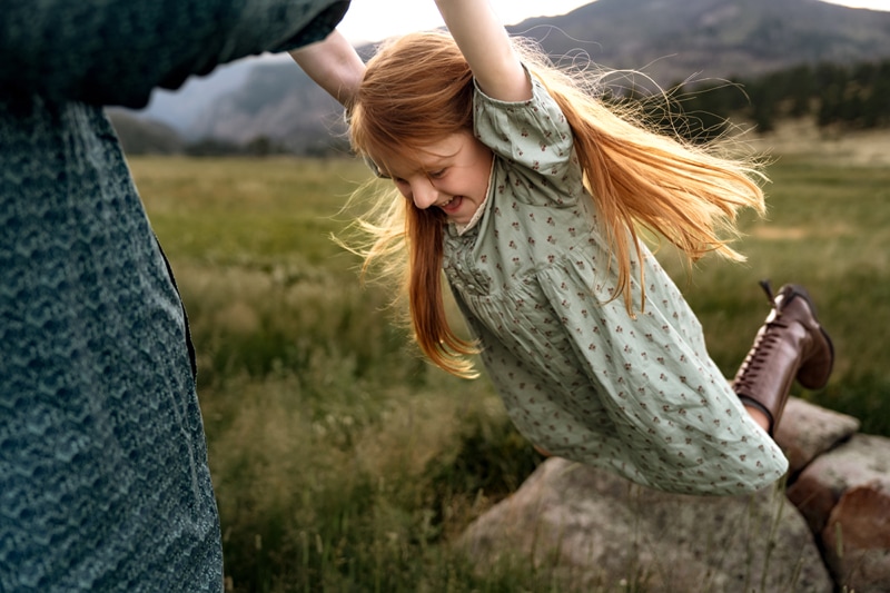 Family Photographer, a little girl swings in the air as her father spins her in a meadow