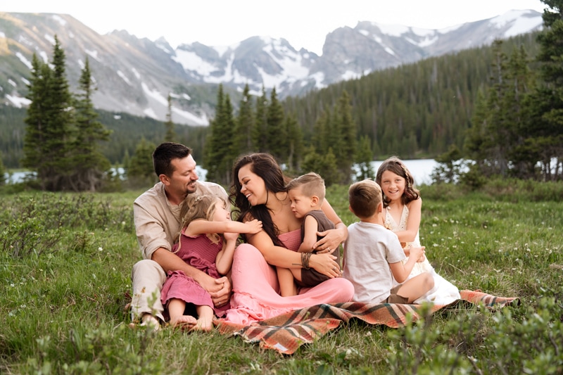 Family Photographer, a mother, father, and their four young children sit in meadows before the mountains