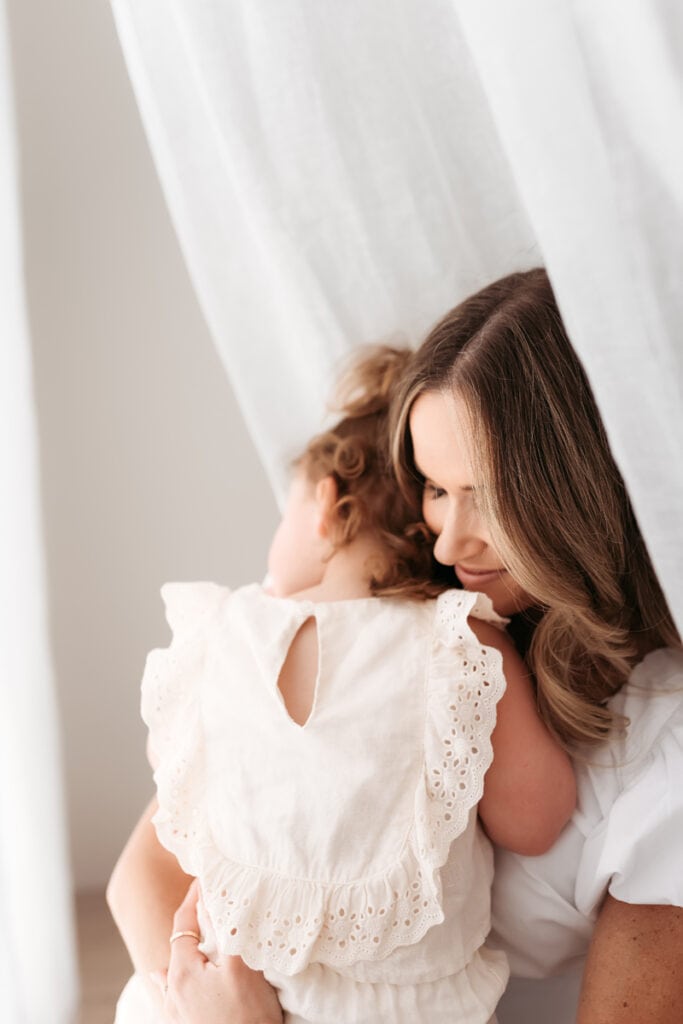 Family Photographer, a mother holds and hugs her baby girl inside