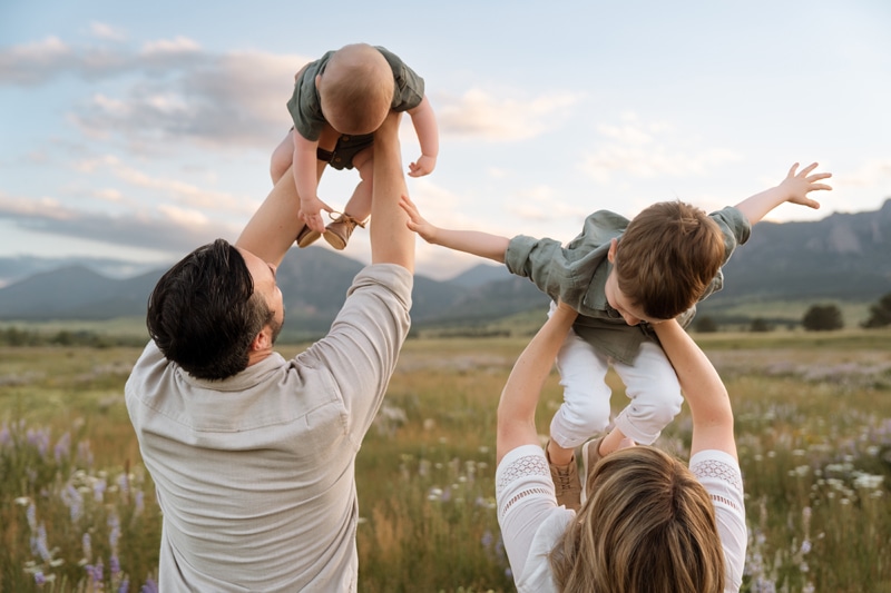 Family Photographer, a dad holds baby in the air and a mother holds her son in a meadow