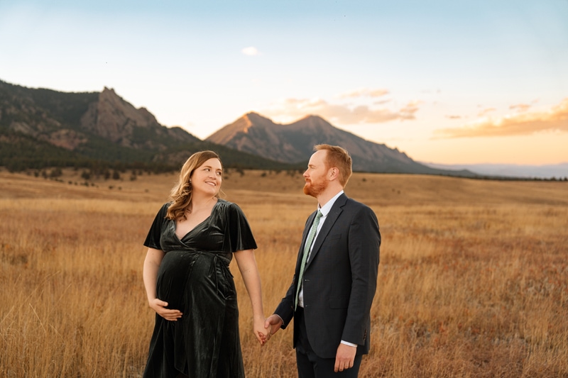 Family Photographer, a pregnant woman and her husband walk together in dry grass before the mountains