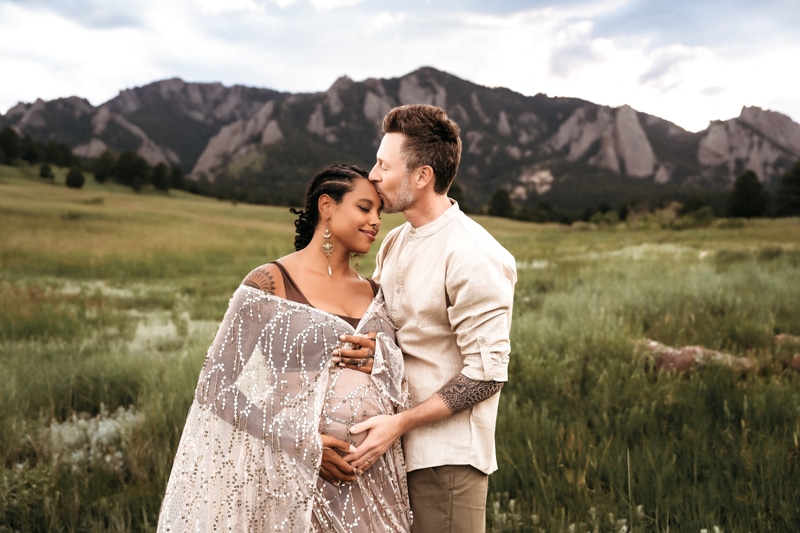 Family Photographer, a pregnant woman leans in her husband before a mountain scape.