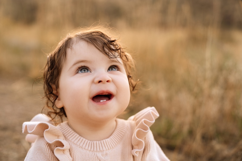 Family Photographer, a baby smiles in a dry grassy field